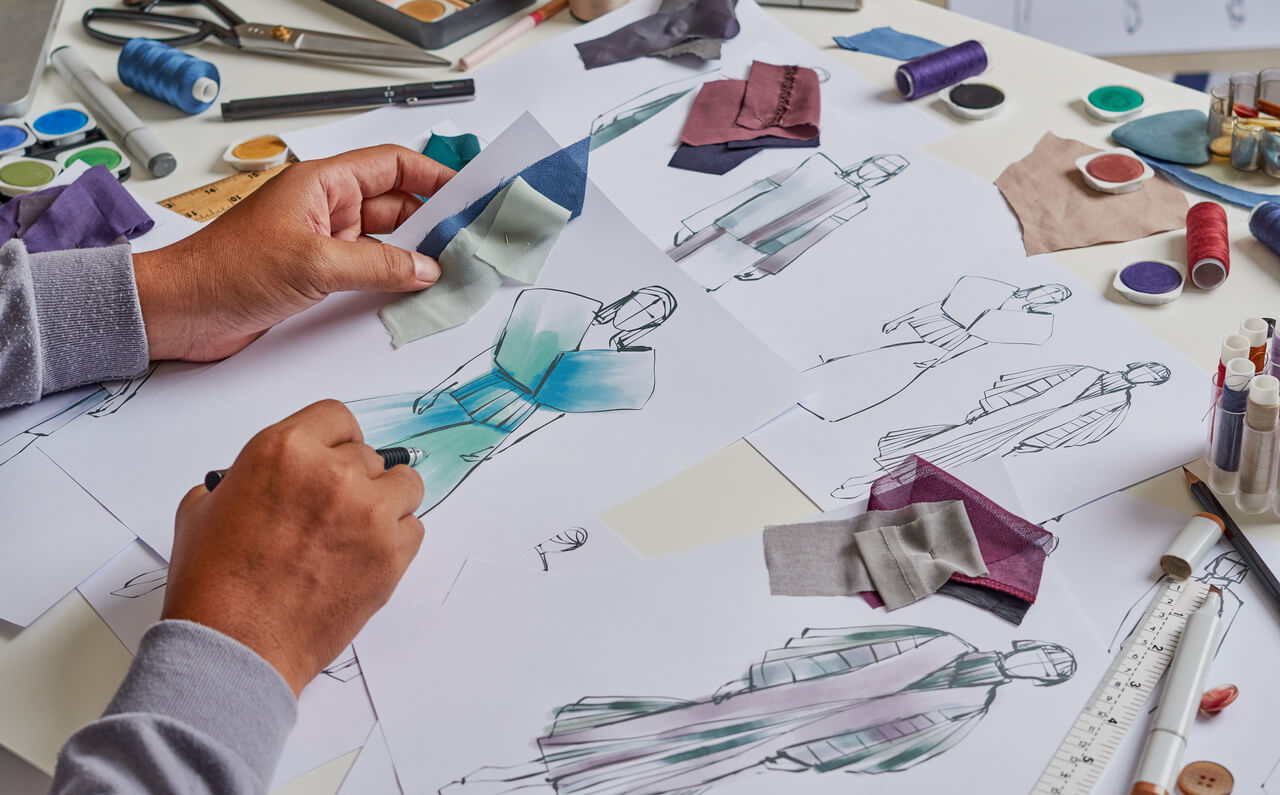 Studente di moda che realizza schizzi e bozzetti con tessuti campione, rappresentando creatività e formazione nelle migliori scuole di moda italiane.